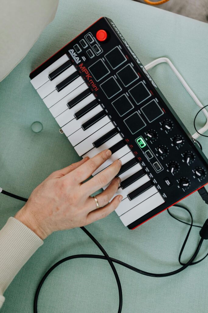 Person's hand playing on a MIDI keyboard controller from a top view in a modern studio setting.